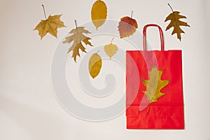 Red paper shopping bag with autumn leaves on beige background. Autumn discounts and sales. Shopping dayRed paper shopping bag with