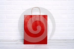 Red paper shopping bag on white brick wall background. Copy space for text