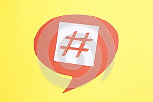 Red paper speech bubble with hashtag symbol on yellow background, top view