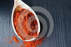 Red paprika powder in a wooden spoon. Dark background, close up
