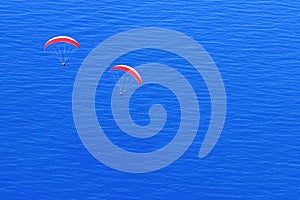 Red parachutes in the sky above the blue sea. Image in the style of minimalism.
