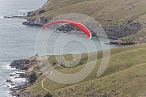 Red paraglider in flyght over ocean shore at Taylors Mistake bay, Christchurch, New Zealand