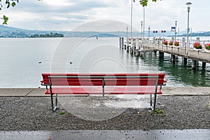 Red park bench on a lake shore with a view of the harbor pier