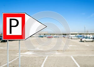 Red parking sign with arrow pointing with blurred cars at the background