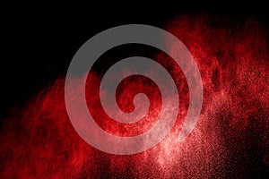 Red particles explosion on black background. Freeze motion of red dust splash on dark background