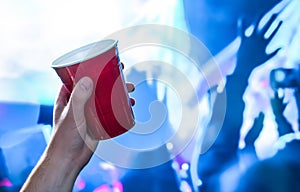 Red party cup in hand in night club, bar or college student event. Plastic beer mug. People having fun in blue nightclub disco.