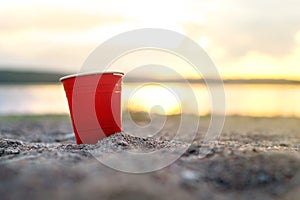 Red party cup in sand at sunset.