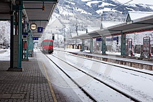 Red passenger high-speed train pulls up to stop at deserted snow-covered railway station in mountains. Concept of transport,