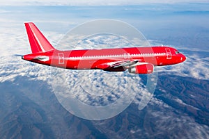 Red passenger plane flies in the sky above the cumulus clouds