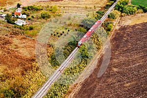 Red passenger train traveling through countryside, aerial view