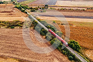 Red passenger train traveling through countryside, aerial view