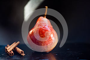 Red pear and whole cinnamon on a dark background in a low key