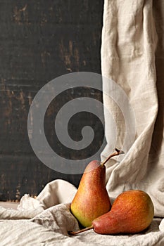 Red pears on linen tablecloth, on black abstract background. Fall fine art still life