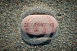 Red pebble stone alone on sand with word Quarantine carved on it