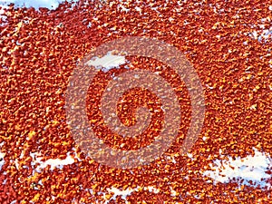 Red pebbles or rubberized textured material and white snow on it. Background, texture, frame, copy space. Contrast of