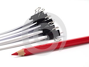 Red pencil in front of several stacks of paper held by binder clips on white background