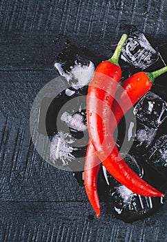 Red pepper and ice on a black wood background, fresh hot food on vintage table, freeze cold cube ice mock up top view