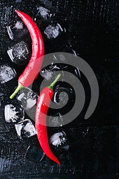 Red pepper and ice on a black wood background, fresh hot food on vintage table, freeze cold cube ice, mock up top view