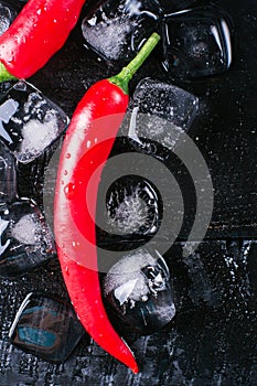 Red pepper and ice on a black wood background, fresh hot food on vintage table, freeze cold cube ice, mock up top view