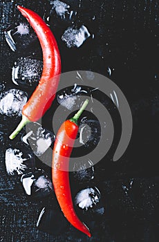 Red pepper and ice on a black wood background, fresh hot food on vintage table, freeze cold cube ice mock up top view