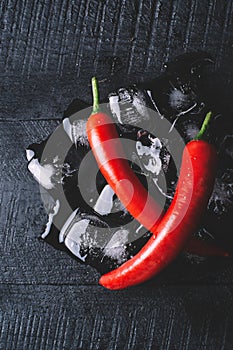 Red pepper and ice on a black wood background, fresh hot food on vintage table, freeze cold cube ice, mockup top view