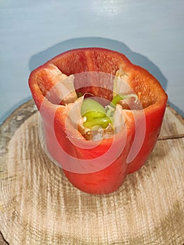 Red pepper that inside there are green peppers next to the seeds. Leaning on a wooden trunk of a tree. White background.