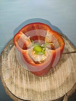 Red pepper that inside there are green peppers next to the seeds. Leaning on a wooden trunk of a tree. White background.