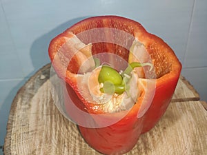 Red pepper that inside there are green peppers next to the seeds. Leaning on a wooden trunk of a tree. White background.