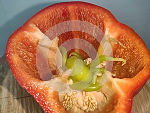 Red pepper that inside there are green peppers next to the seeds. Leaning on a wooden trunk of a tree. White background.