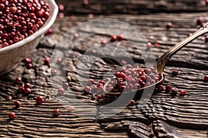 Red peppercorn in bowl and spoon on oak table