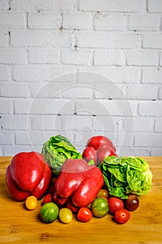 Red peppers, green salad and cherry tomatoes in front of empty white brick wall
