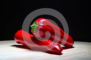 Red peppers lie on a wooden board on a black background