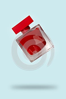 Red perfume bottle flying on a blue background. The concept of a favorite fragrance