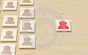 Red person symbol next to group of people symbols on table background, concept of standing out, being different, inclusivity or