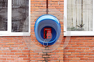 Red phone public apparatus protected blue booth on the brick wall of the house.