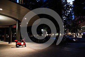 A red piaggio vespa under the light during night