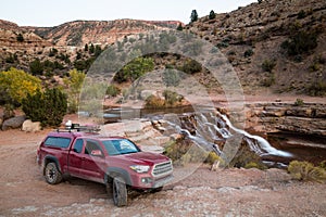 Red pickup camping rig on rocky trail near waterfall in southern