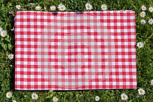 Red picnic blanket. Red checkered picnic cloth on a flowering meadow with daisy flowers. Beautiful backdrop for your product