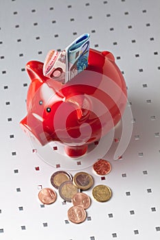 Red piggy bank with euro notes and coins