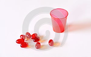 Red pill cup and red pills capsule on white background.