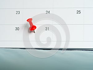 Red pin push on day 31 of end month on white calendar. Mark this day as salary date. Concept of meeting appointment reminder