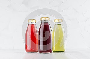 Red, pink, green fruit juices set in glass bottles with cap mock up group on white wood table in light interior, template for pack