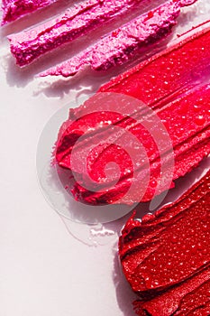 Red and pink lipstick swash with water drops closeup. Make-up sample isolated. Beauty swash texture