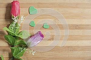 Red and pink plastic roses and small hearts on a wooden table for the concept of love