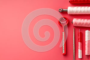 Red pink sewing tools and thread spools on pink background