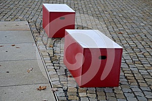 Red plastic benches in the shape of blocks with handles. The square is paved with granite cubes. sandy surface. built around a squ