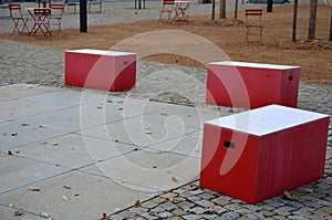 Red plastic benches in the shape of blocks with handles. The square is paved with granite cubes. sandy surface. built around a squ