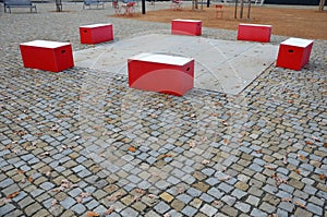 Red plastic benches in the shape of blocks with handles. The square is paved with granite cubes. sandy surface. built around a squ