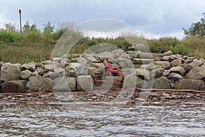 A red plastic chair on sandstone steps on a seawall above the beach in Nova Scotia