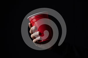 Red plastic cup with a hand in the dark.